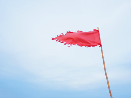 Tearing red flag waving against blue sky background. Warning sign on the beach.の写真素材