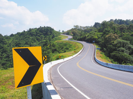 black and yellow directional warning arrow sign on a dangerous curve road across mountain.の写真素材