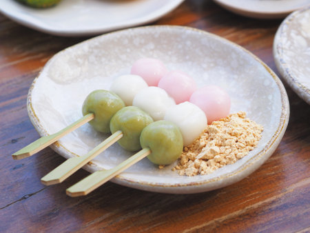 Colorful Dango or Japanese rice dumplings with brown sugar and soybean powder on ceramic plate.