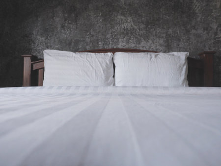 Two white pillows and blanket on wooden vintage bed over grunge painted brush concrete wall in the bedroom.の写真素材