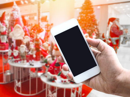 Hand holding mobile phone over abstract blurred background of decoration for xmas or festive party at department store.の写真素材