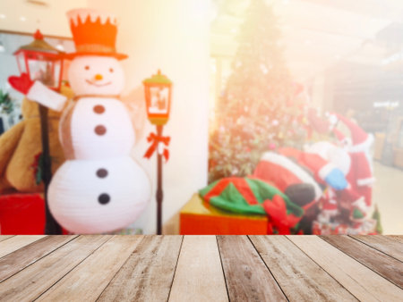 Wooden table top over  abstract blurred background of snowman decoration for Christmas holiday or festive party at department store. Montage picture style to display the product. Shopping concept.の写真素材