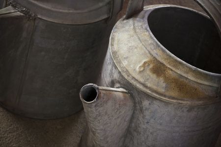 Two rustic old watering cans on a concrete floor.の写真素材