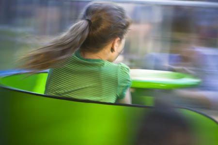 Pony-tailed girl on a bright green twirling carnival ride. Motion blur was captured in-camera with slow exposure and is intentional.の写真素材