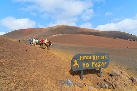 Entrance sign to Timanfaya National Park with caravan of camels in distance, Lanzarote, Canary Islands, Spainの写真素材