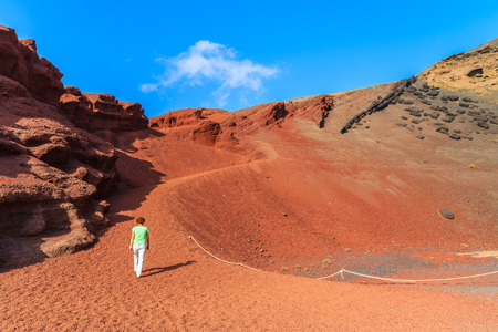 Young woman tourist walking on red lava hills near Lago Verde lake, El Golfo, Lanzarote, Canary Islands, Spainの写真素材