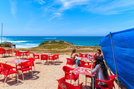 PRAIA DO AMADO BEACH, PORTUGAL - MAY 15, 2015: tourists sitting in a cafe on Praia do Amado beach with ocean in background, Algarve region, Portugal.のeditorial素材
