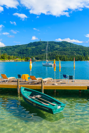 WORTHERSEE LAKE, AUSTRIA - JUN 20, 2015: tourist boats and sunchairs with umbrellas on wooden pier of beautiful alpine lake Wortのeditorial素材