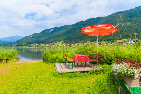 WEISSENSEE LAKE, AUSTRIA - JUL 6, 2015: umbrellas with sunbeds on beach at Weissensee lake in summer landscape of Alps Mountainsのeditorial素材
