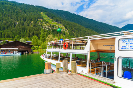 WEISSENSEE LAKE, AUSTRIA - JUL 6, 2015: tourist boat mooring to pier on shore of Weissensee lake in summer landscape of Alps Mountainのeditorial素材