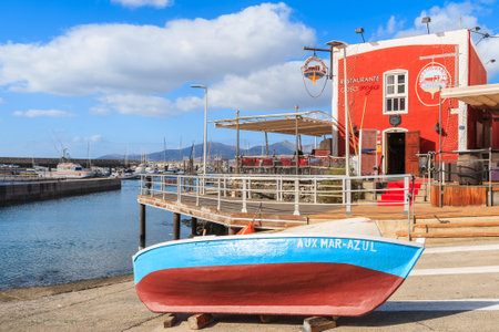 PUERTO DEL CARMENT PORT, LANZAROTE - JAN 17, 2015: colorful fishing boat in front of red restaurant building in Puerte del Carmen port. This town is popular holiday destination on Lanzarote island.のeditorial素材