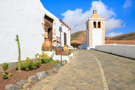 Village street with traditional houses with flower pots in front and tower of Cathedral Santa Maria de Betancuria in the background, Betancuria village, Fuerteventura, Canary Islands, Spainの写真素材