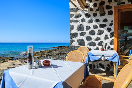 MORRO JABLE, FUERTEVENTURA - FEB 7, 2014: tables and chairs of a restaurant on coast of Morro Jable town. Building is made of lava stones, traditional type of construction on the island.のeditorial素材