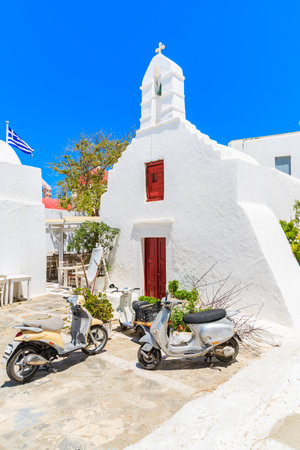 MYKONOS TOWN, GREECE - MAY 16, 2016: Two scooters parked in front of a typical white church with red doors in Mykonos town, Cyclades islands, Greece.のeditorial素材