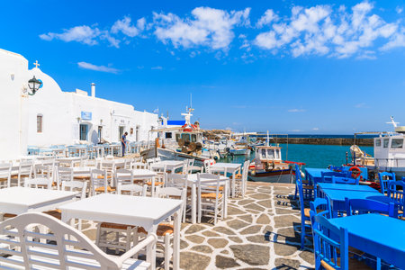 NAOUSSA PORT, PAROS ISLAND - MAY 20, 2016: Tavern tables and typical white Greek buildings in Naoussa port, Paros island, Cyclades, Greece.のeditorial素材