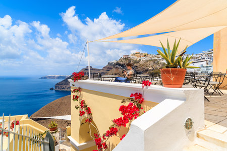 FIROSTEFANI, SANTORINI ISLAND - MAY 22, 2016: tourist girl sitting on a terrace looking at pictures taken of Santorini island, Greece.のeditorial素材