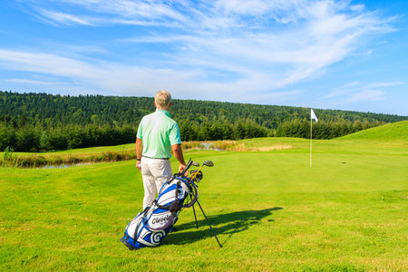 ARLAMOW GOLF COURSE, POLAND - AUG 3, 2014: mature man plays golf on sunny summer day in Arlamow Hotel. This luxury hotel was owned by Poland's government and is located in Bieszczady Mountains.のeditorial素材