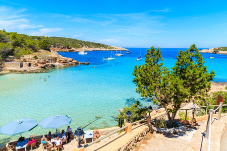 CALA PORTINATX BAY, IBIZA ISLAND - MAY 16, 2017: people sitting in restaurant of on shore of Cala Portinatx bay, Ibiza island, Spain.のeditorial素材