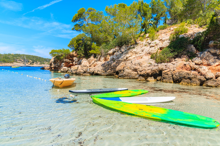 Yellow boat and surfing boards on idyllic Cala Portinatx beach and cliff rocks with pine trees in background, Ibiza island, Spainの写真素材
