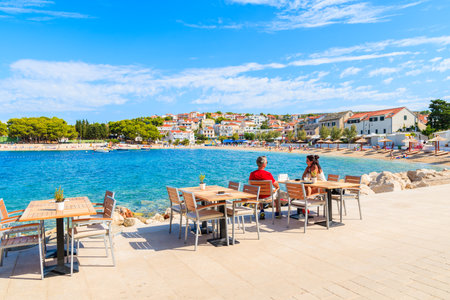 PRIMOSTEN, CROATIA - SEP 5, 2017: Couple of tourists sitting in seaside bar in Primosten town enjoying summer vacation, Dalmatia, Croatia.のeditorial素材
