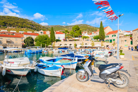 BOL PORT, BRAC ISLAND - SEP 8, 2017: Scooter parking in Bol port with colorful fishing boats, Brac island, Croatia.のeditorial素材