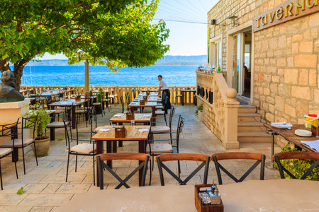 BOL PORT, CROATIA - SEP 13, 2017: Waitress setting tables in coastal restaurant in Bol port on sunny summer day, Brac island, Croatia.のeditorial素材