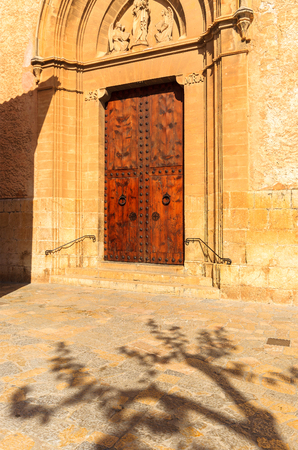 Wooden door cathedral building tree trunk shade, Pollenca, Majorca island, Spainの写真素材