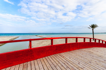 Red wooden footbridge sand beach sea white clouds blue sky palm tree, Alcudia, Majorca island, Spainの写真素材