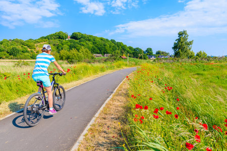 Young woman cyclist riding bicycle on route from Baabe to Moritzdorf village in countryside spring landscape, Ruegen island, Baltic Sea, Germanyのeditorial素材