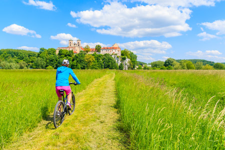 Young woman cyclist riding bike on green meadow and view of Tyniec monastery on sunny spring day, Cracow city, Polandのeditorial素材