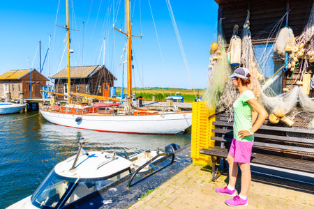GAGER PORT, RUGEN ISLAND - MAY 29, 2018: Young woman tourist standing in front of traditional wooden houses in Gager port, Ruegen island, Baltic Sea, Germany.のeditorial素材