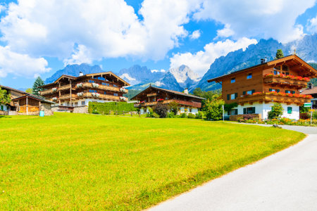 Road and traditional alpine houses in village of Going am Wilden Kaiser on beautiful sunny summer day with Alps mountains in background, Tirol, Austriaのeditorial素材