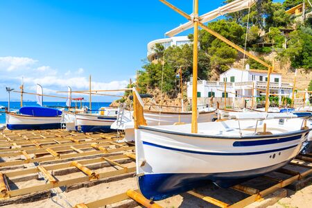 Traditional white and blue colour fishing boat on Sa Riera beach with sea and village houses in background, Costa Brava, Spainの写真素材