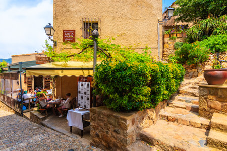 TOSSA DE MAR OLD TOWN, SPAIN - JUN 3, 2019: People dining in restaurant in old town of Tossa de Mar with stone houses, Costa Brava, Spain.のeditorial素材