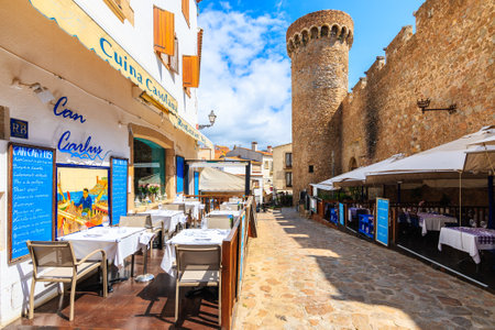 TOSSA DE MAR, SPAIN - JUN 6, 2019: Restaurant tables in beautiful old town of Tossa de Mar which is a seaside resort on Costa Brava, Spain.のeditorial素材