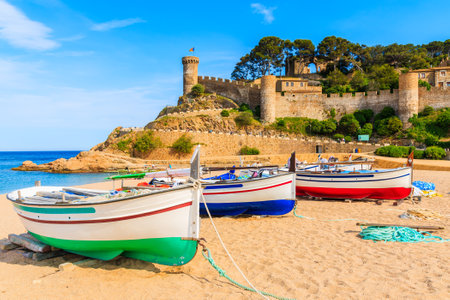 Fishing boats on golden sand beach in bay with castle in background, Tossa de Mar, Costa Brava, Spainのeditorial素材