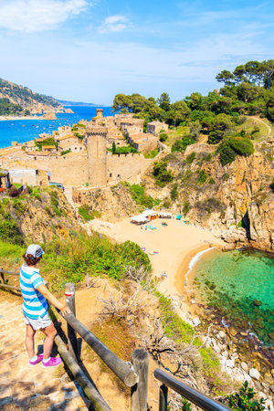 Young woman tourist standing on coastal path and looking at sandy beach and bay in Tossa de Mar town, Costa Brava, Spainのeditorial素材