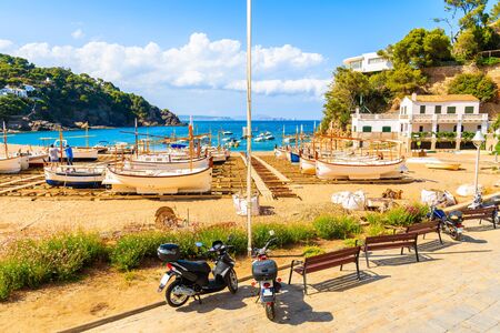 Scooters parking on coastal promenade and view of fishing boats on beach in beautiful Sa Riera village, Costa Brava, Catalonia, Spainの写真素材