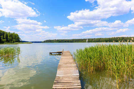 Wooden pier and grass on lake Nidzkie shore on sunny summer day with beautiful clouds on blue sky, Mazury Lake District, Polandの写真素材