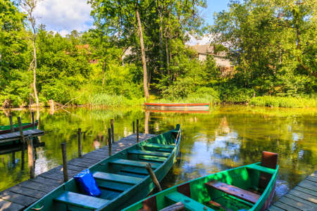 Wooden boats at pier on bank of Krutynia river where tourists do kayaking during summer months,...