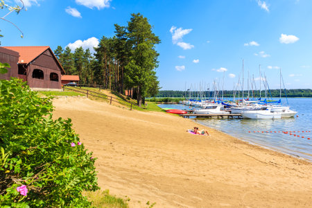 KARWICA BEACH, POLAND - JUN 25, 2020: Couple of people relaxing on beach at lake Nidzkie shore in Krzyze village port on sunny summer day, Mazury Lake District, Poland.のeditorial素材