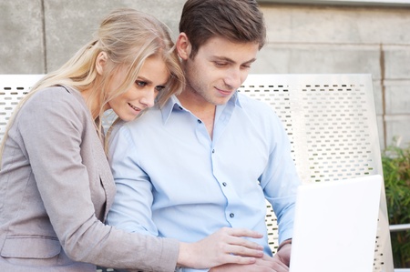 Portrait of a happy young professional couple using laptop sitting outsideの写真素材