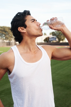 Handsome, young latino athlete drinking water standing on athletic fieldの写真素材
