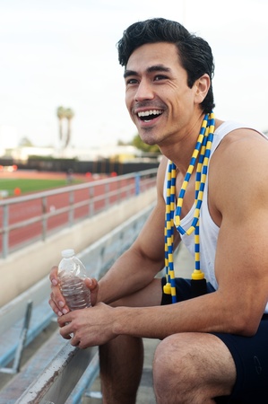 Handsome, young latino athlete sitting in the bleachers with water and jumpropeの写真素材