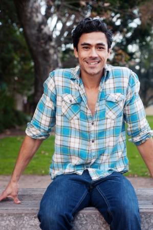 Happy young man sitting in a park smiling at the camera Happy young man sitting in a park smiling at the camera