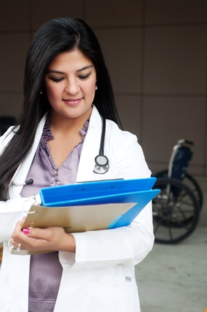 Portrait of young female doctor standing with wheelchair and holding a clipboardの写真素材