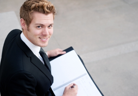 Portrait of a happy young businessman with notepad sitting outsideの写真素材