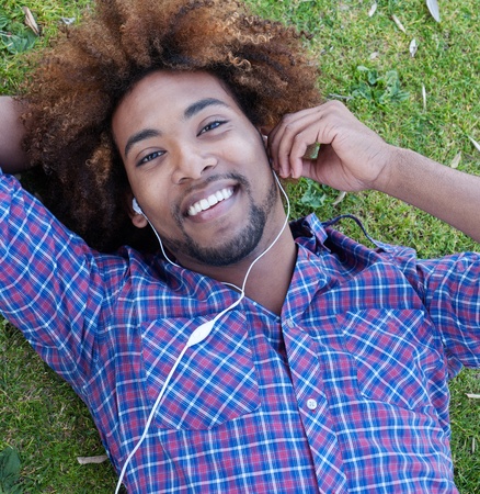 young, happy african american male lying in grass listening to musicの写真素材