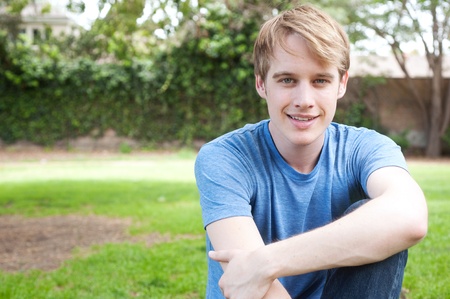  young male student sitting in the grass and smilingの写真素材