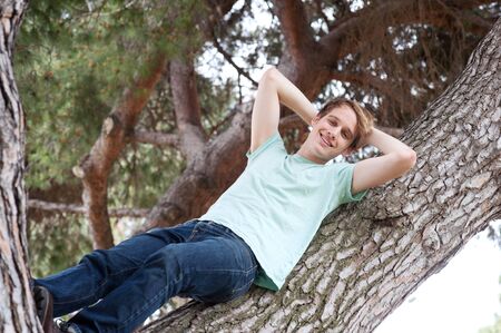 portrait of a young male relaxing on a tree outside in a parkの写真素材